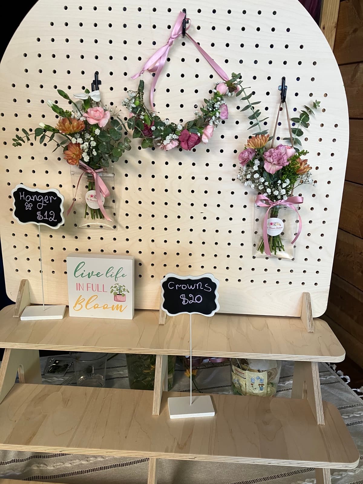 Flower crowns and hair pieces displayed on a pegboard with 'Live life in full bloom' sign